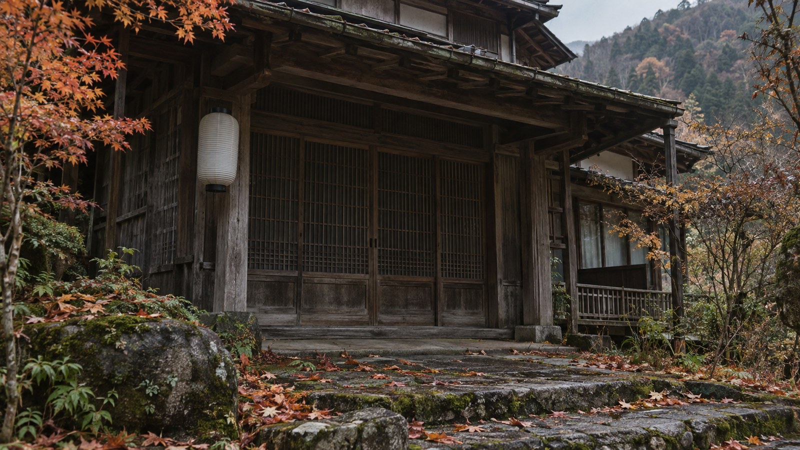 秋の山あいの古い木造旅館の入口。戸は閉まり、提灯は消え、石段に落ち葉がたまっている
